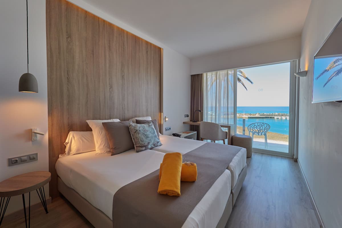 A modern hotel room with a large bed, a desk, and a view of the beach.