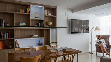 Una sala de estar moderna con comedor, muebles de madera, un televisor de pantalla plana y una persona leyendo un libro.