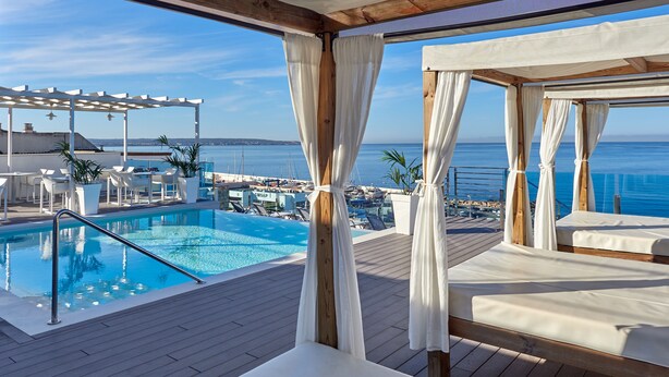 A poolside area with a wooden deck, lounge chairs, and a view of the sea.
