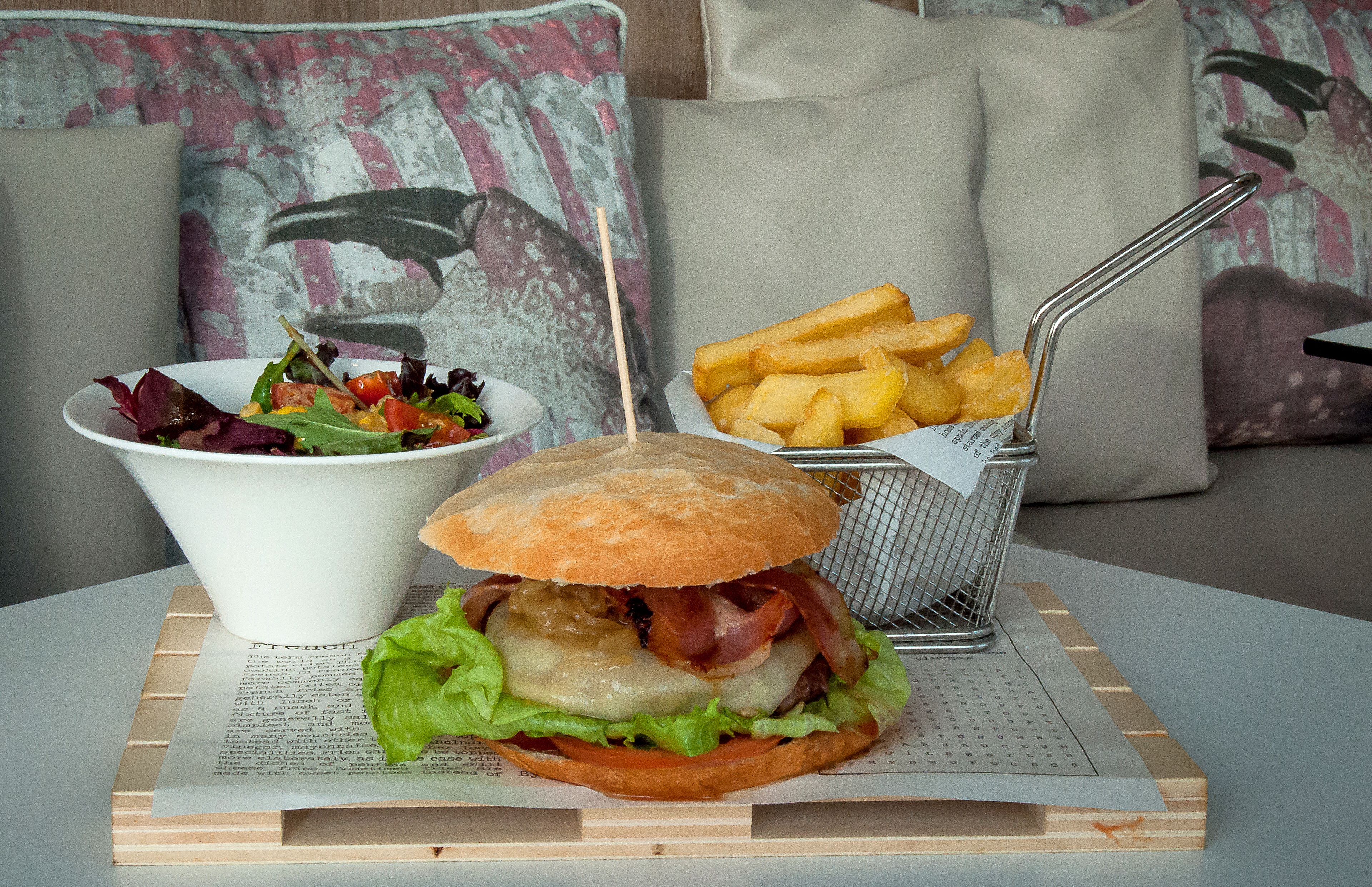 A meal consisting of a burger, fries, and a salad on a wooden board.
