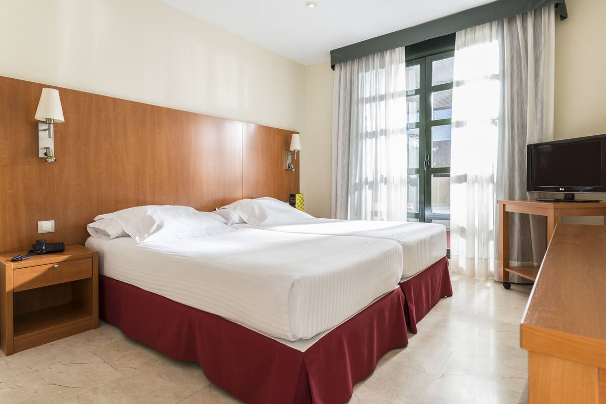 Habitación de hotel con dos camas, un escritorio, un televisor y una ventana con cortinas.