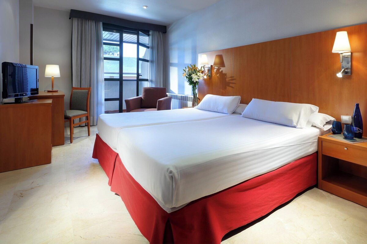 Ein Hotelzimmer mit einem großen Bett, einem Fernseher, einem Schreibtisch und einem Fenster mit Blick.