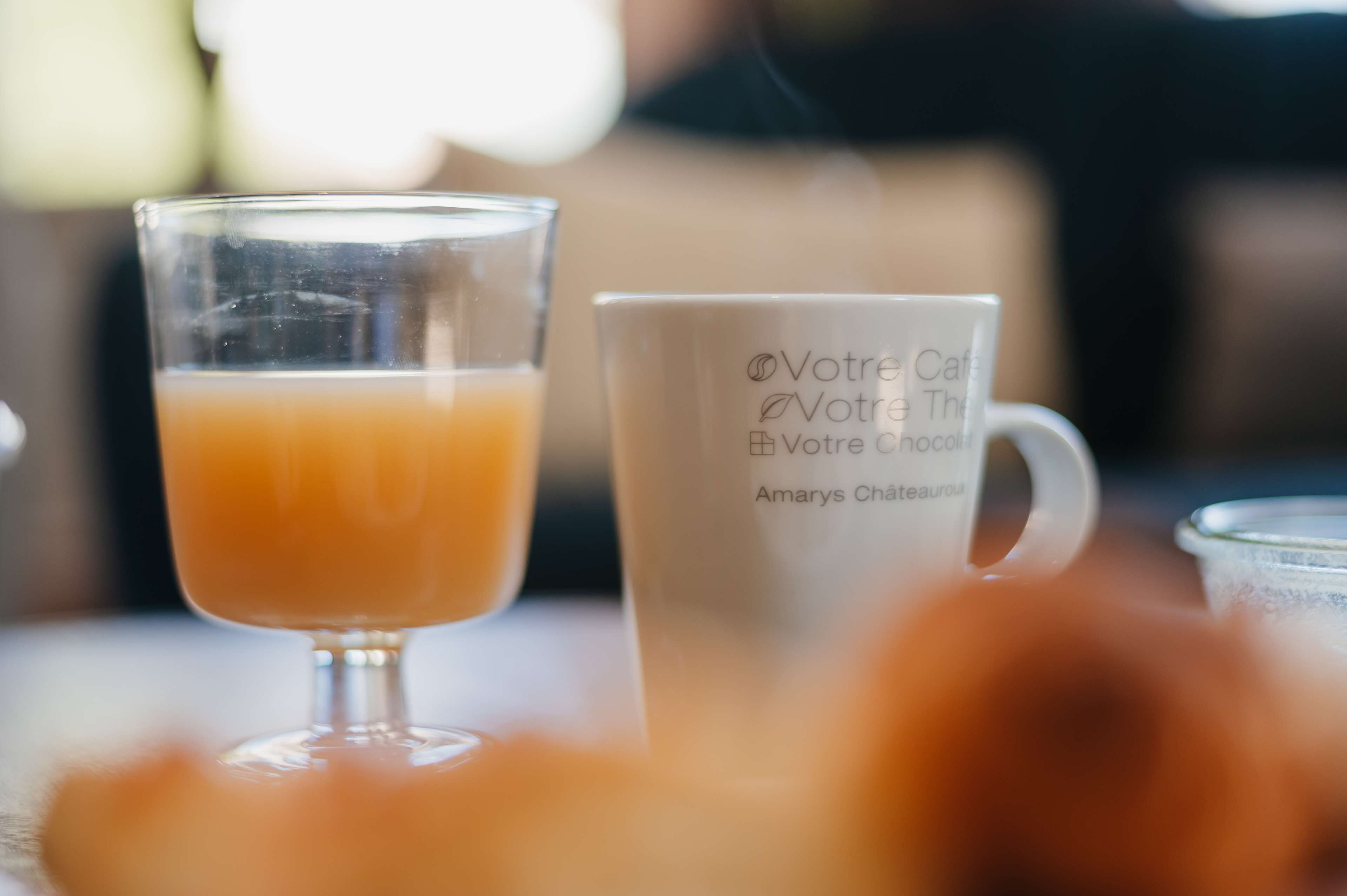 A glass of orange juice and a white mug with text on it.