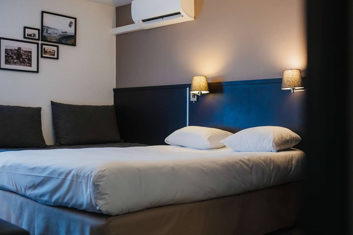 A neatly made bed with white linens and two pillows, a dark headboard, and two wall-mounted lamps with textured shades.