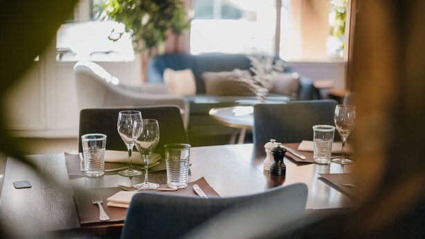A dining table set with glasses and cutlery, a salt shaker, and a menu.