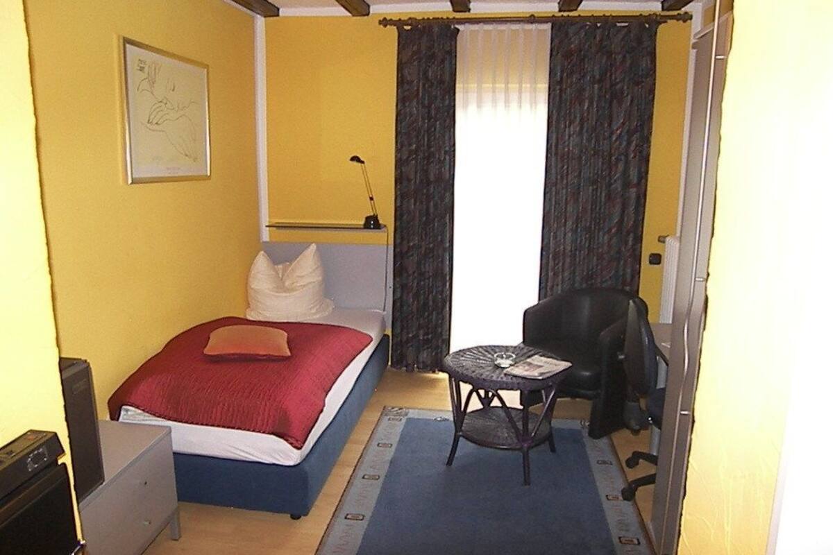 A small room with a bed, a desk, a chair, and a window with curtains.