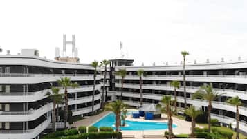 Hotel de diversos pisos amb una piscina central envoltada de palmeres i una zona ajardinada.