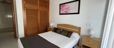 Un dormitorio con cama, armario de madera, mesitas de noche y un cuadro en la pared.