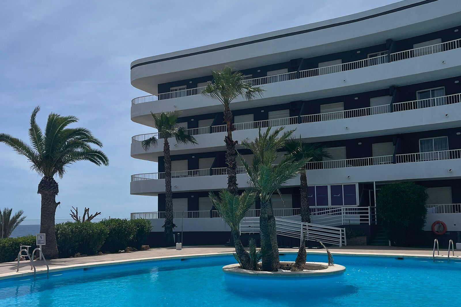 Un hotel de varios pisos con piscina rodeada de palmeras.