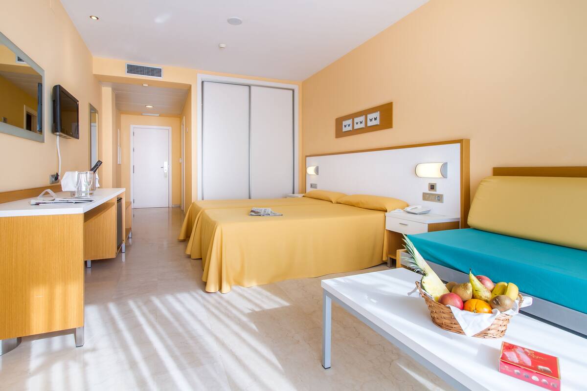 A hotel room with two beds, a desk, a TV, and a fruit basket on the nightstand.
