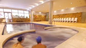 Una piscina interior con pared de piedra y sillas a un lado.