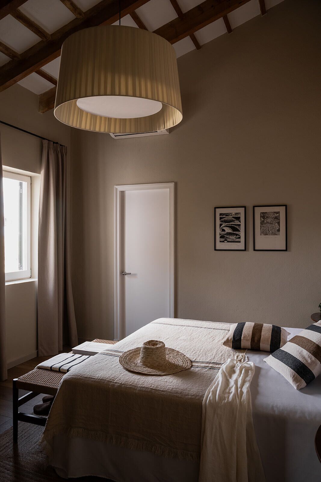 A bedroom with a bed, a hanging lamp, a door, and two framed pictures on the wall.