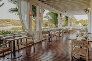An outdoor dining area with wooden tables and chairs, surrounded by white railings and palm trees. - Binissaida Boutique Hotel (Es Castell)