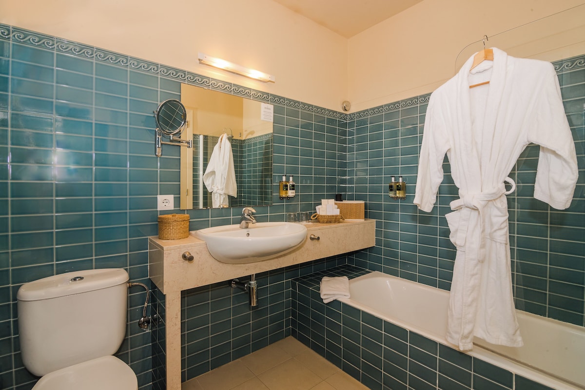 A bathroom with a white sink, a bathtub, and a white robe hanging on the wall.