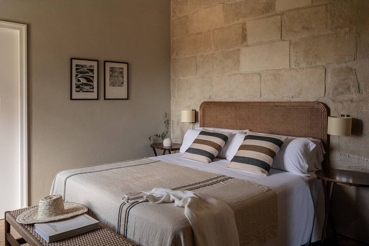 Une chambre à coucher bien aménagée, avec un grand lit, deux tables de chevet, une tête de lit en osier et deux œuvres d’art encadrées accrochées au mur.