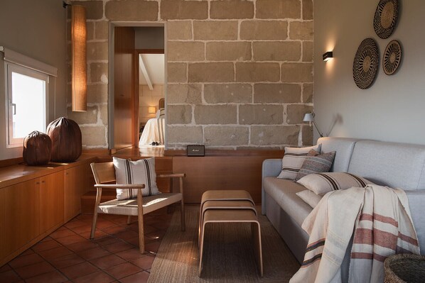 A cozy living room with a stone wall, a sofa, a wooden bench, and a chair.