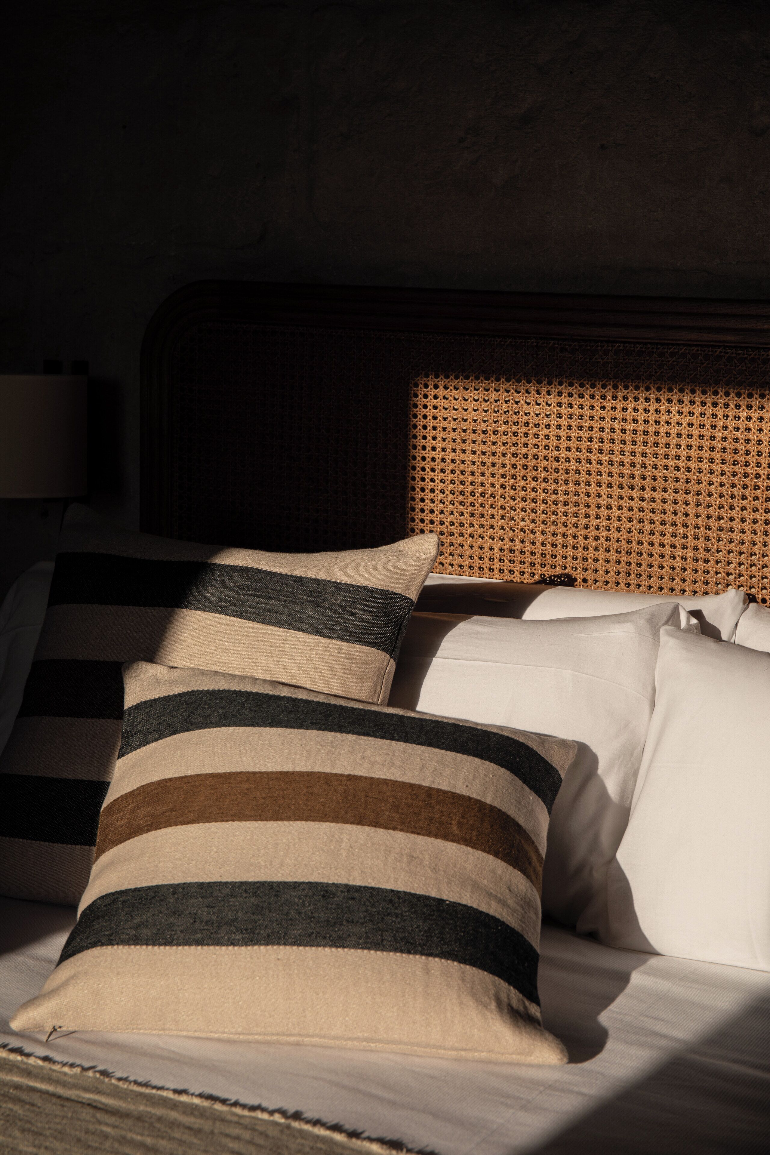 A bed with striped pillows and a woven headboard.
