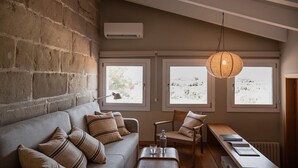 Une pièce chaleureuse avec un mur en pierre, un canapé orné de coussins à rayures, une chaise en bois, une table avec une bouteille et des verres, et un luminaire suspendu.