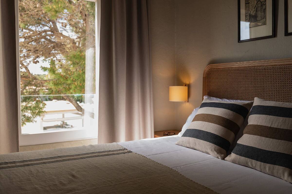 Une chambre d’hôtel avec un lit, une table de chevet avec une lampe, une fenêtre avec des rideaux et une vue sur l’extérieur.