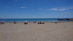 Una playa con gente relajándose bajo sombrillas y tumbonas.