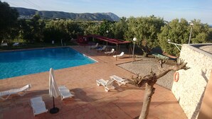 Una piscina con sillas de descanso y sombrillas, rodeada de árboles y vistas a montañas.