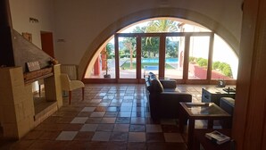 Una habitación amplia con suelo a cuadros, un sofá, una mesa y un gran ventanal con vistas a una piscina y vegetación.