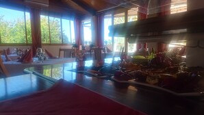 Comedor con mesas dispuestas para una comida, ventanas amplias y vista a zonas verdes al exterior.