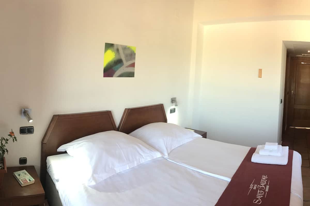 Une chambre d’hôtel avec un grand lit, une armoire en bois, une petite table avec une plante et une porte donnant sur une autre pièce.