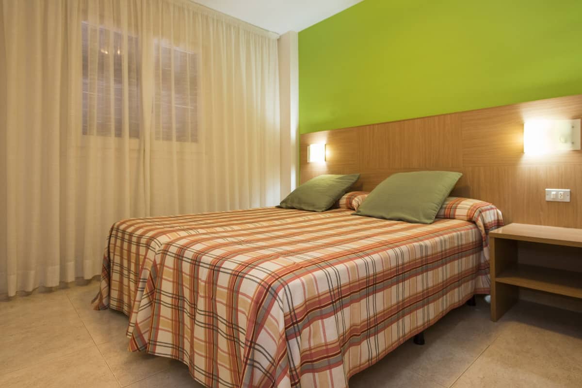 A hotel room with a bed, a nightstand, a green wall, and a window with curtains.