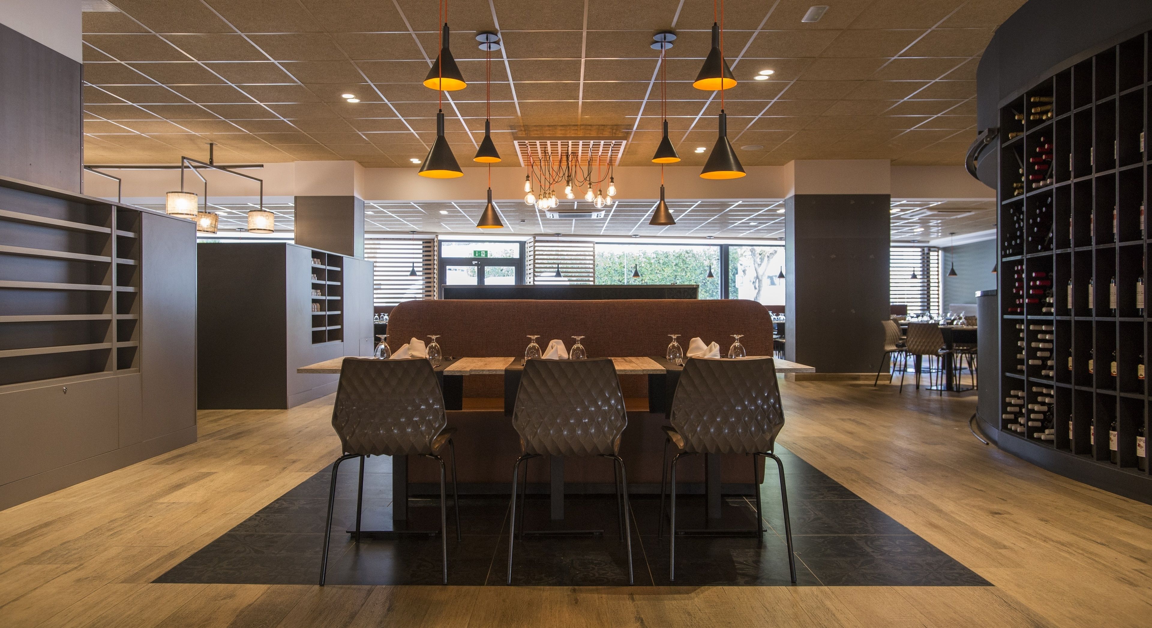 A modern restaurant with a central seating area, a wine rack, and a view of the outdoors.