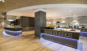A modern buffet setup with a central island, a kitchen area, and a wooden wall. - Apartamentos California (Salou)