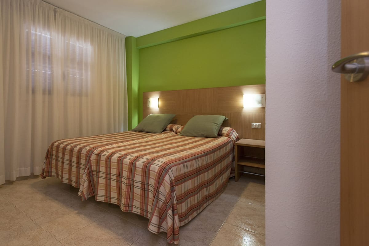 A bedroom with a bed, curtains, a nightstand, and a green wall.
