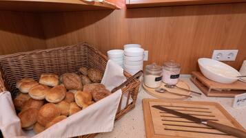 Una encimera de cocina con una cesta de mimbre llena de pan, una tabla de cortar, un cuchillo y un tarro de leche.