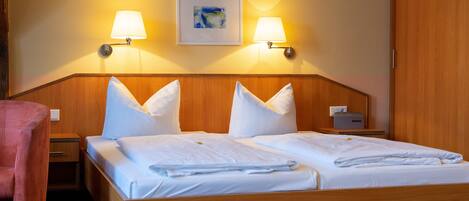 Una cama doble con ropa de cama blanca, dos lámparas de noche, una obra enmarcada sobre la cama y un cabecero de madera.