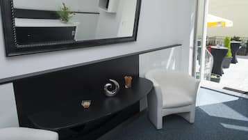 A modern hotel room with a black console table, a white armchair, a large mirror, and a balcony with outdoor seating.