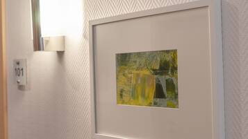 A framed artwork on a textured wall, a wall-mounted light fixture, and a door with a number plate.