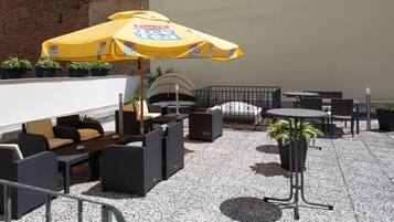 An outdoor patio area with seating arrangements, including sofas and tables, under a yellow umbrella.