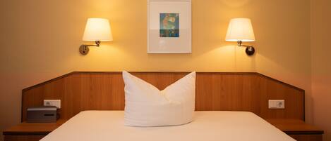 Habitación de hotel con una cama bien hecha, dos lámparas de noche, un cuadro en la pared y una mesita de noche con lámpara.
