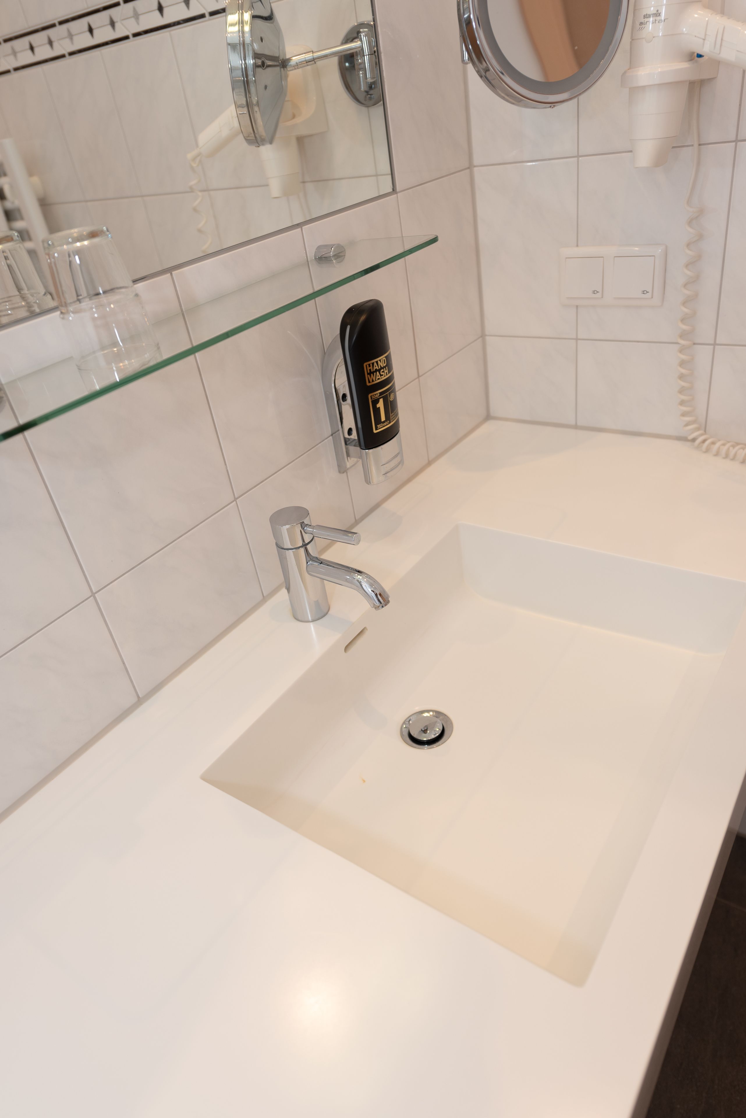 A modern bathroom with a large sink, a glass shelf, a hairdryer, and a mirror.