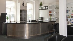 A modern reception area with a curved counter, seating, and a bookshelf. - Hotel Europa (Görlitz)