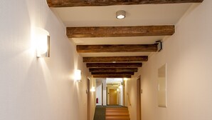 A hallway with a carpeted floor, wooden beams on the ceiling, and wall-mounted lighting fixtures. - Hotel Europa (Görlitz)