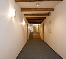 Ein Flur mit Teppichboden, Holzbalken an der Decke und Wandleuchten.