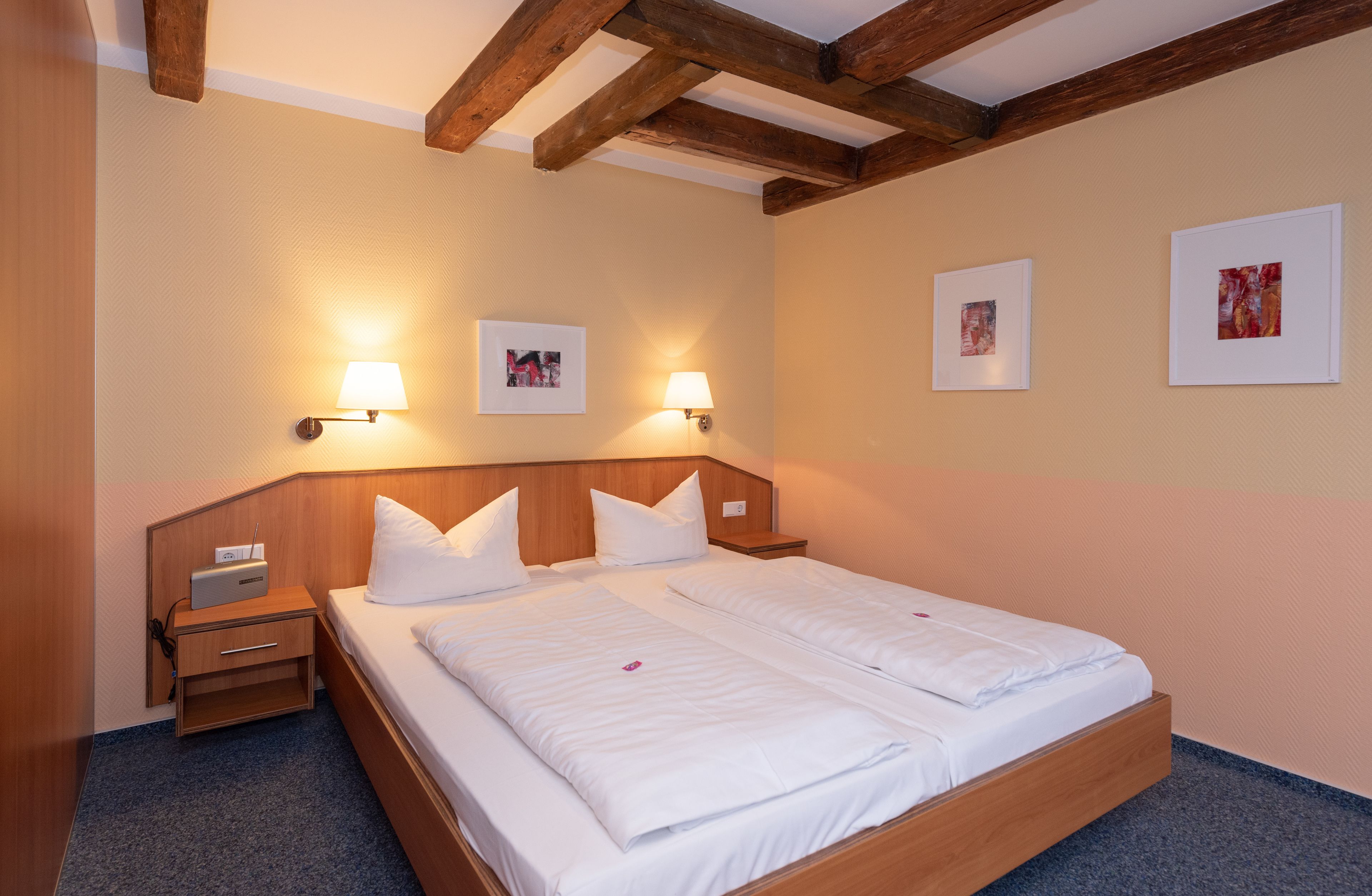 Una habitación de hotel con una cama de madera, dos mesitas de noche y lámparas fijadas a la pared.