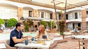 Una pareja cenando en una mesa al aire libre, con una piscina y un patio de fondo.