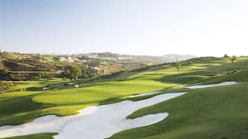 A golf course with bunkers, a flag, and a distant view of buildings.