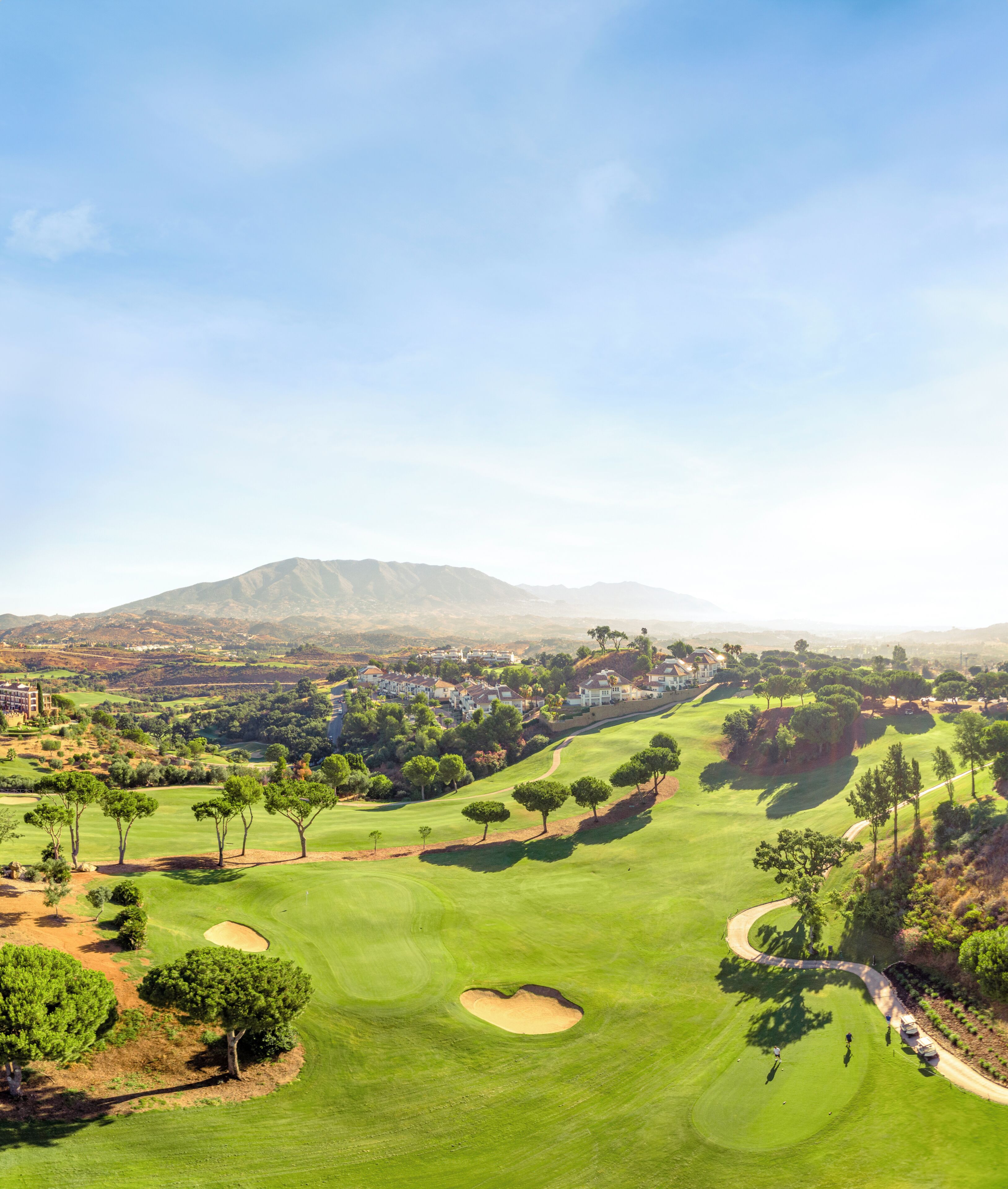 A golf course with a view of a mountain range, a few trees, and a building in the distance.