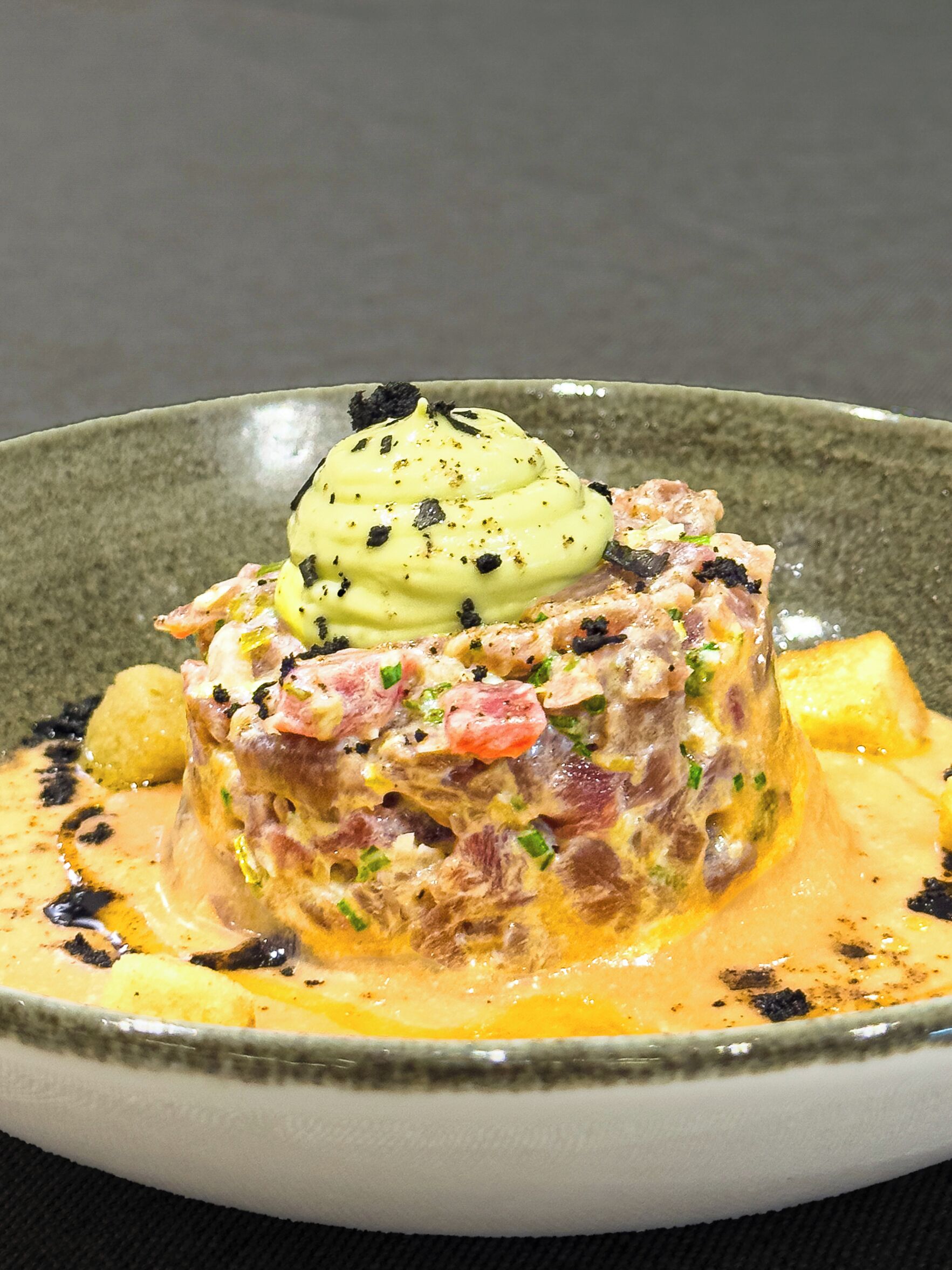 A dish with a creamy sauce, chunks of meat, and a dollop of yellow sauce on top, served on a ceramic plate.