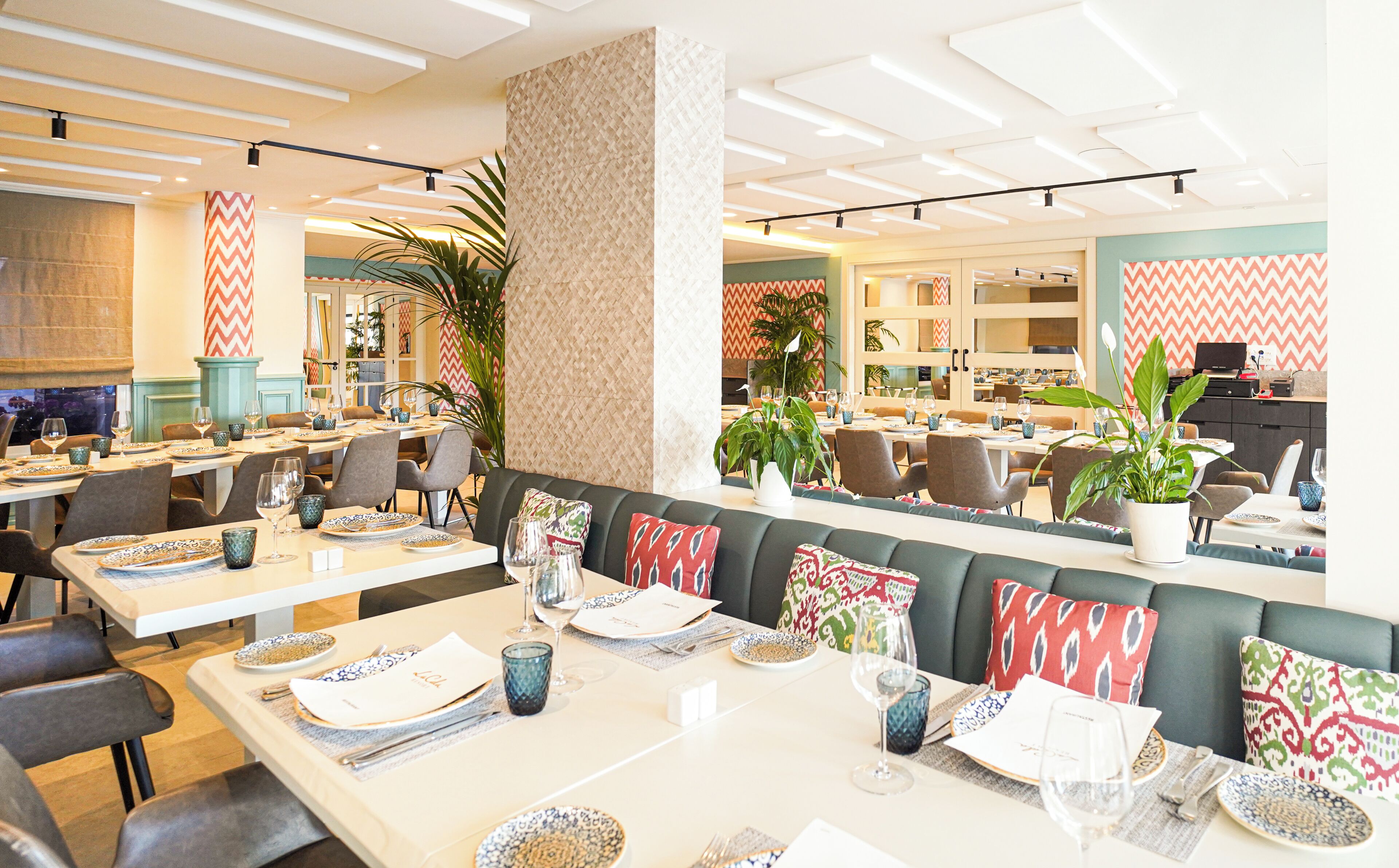 Un restaurant moderne doté de plusieurs espaces de restauration, notamment un espace central avec une table haute et une salle à manger séparée avec des tables individuelles.