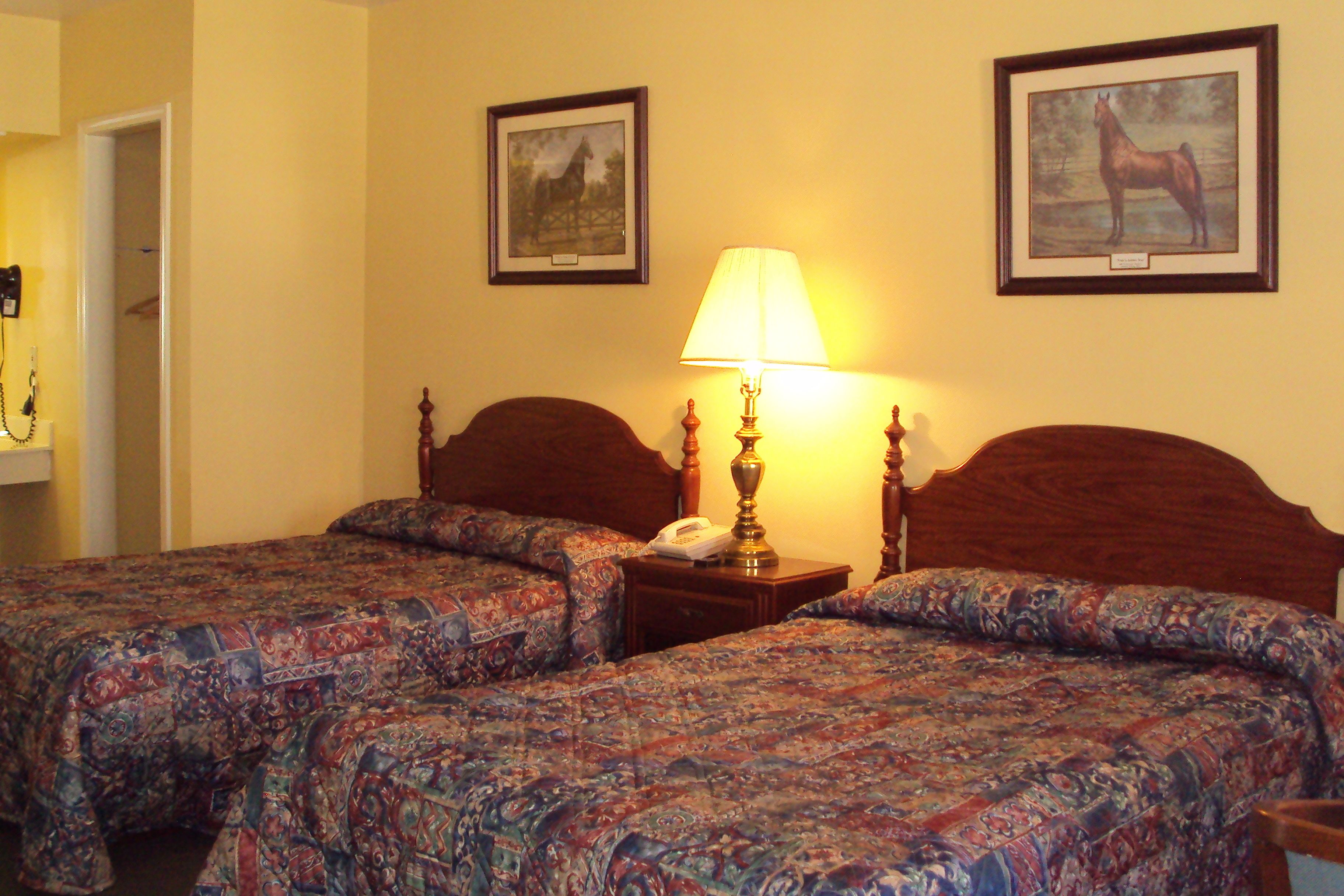 Una habitación de hotel con dos camas, una mesita de noche con lámpara y dos cuadros enmarcados en la pared.