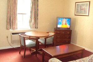 A living room with a round wooden table, two chairs, a television, and a dresser.